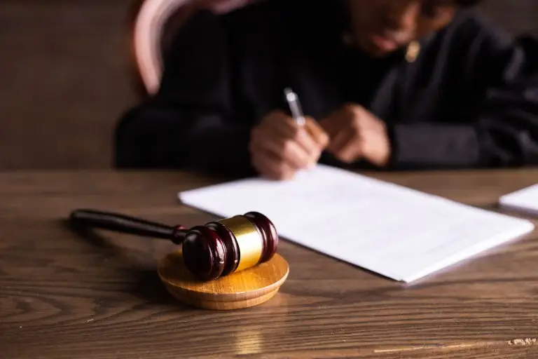 Judge in a courtroom signing a document with a gavel beside her