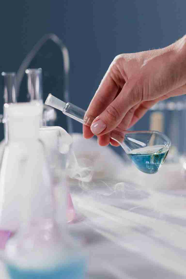 Chemist pouring a blue liquid from a conical flask into a beaker